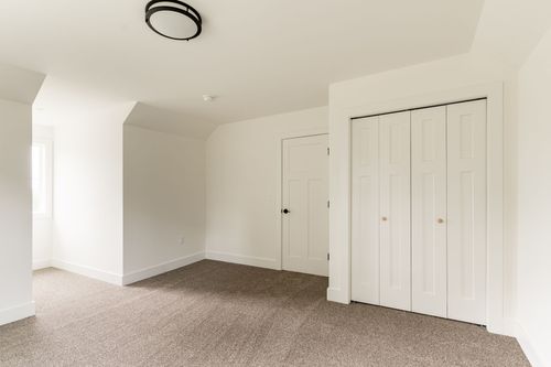 Empty bedroom with a white door, bifold closet and vaulted ceiling