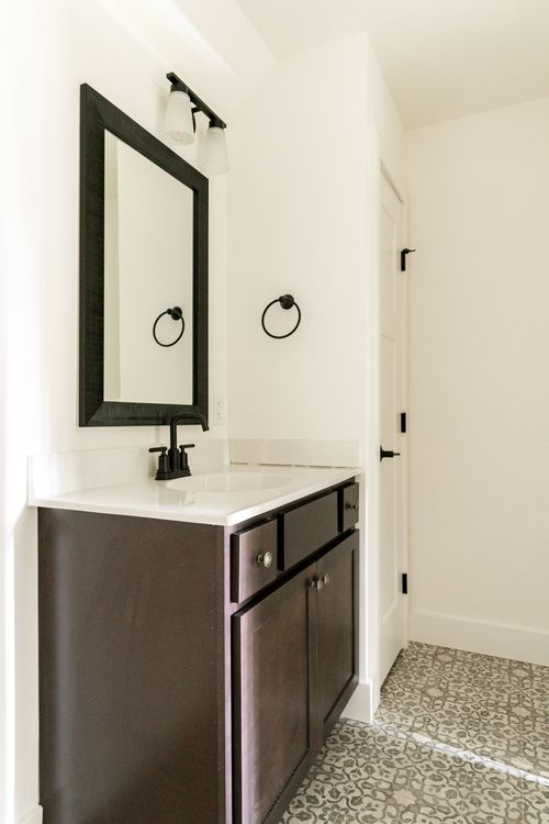 Bathroom vanity with a black-framed mirror, sconces and patterned tile floor