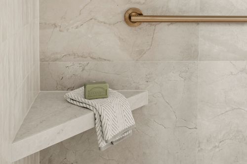 Glass-walled shower with a rain showerhead beside the toilet in a marble tiled bathroom