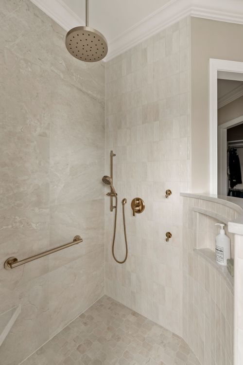 Ceiling-mounted rain showerhead above a marble tiled shower with gold fixtures