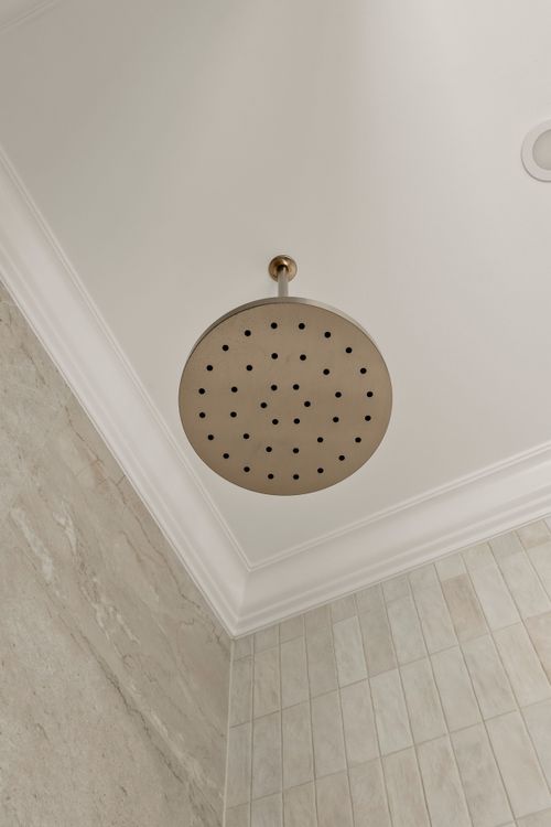 Close view of a ceiling-mounted rain showerhead in a marble tiled shower