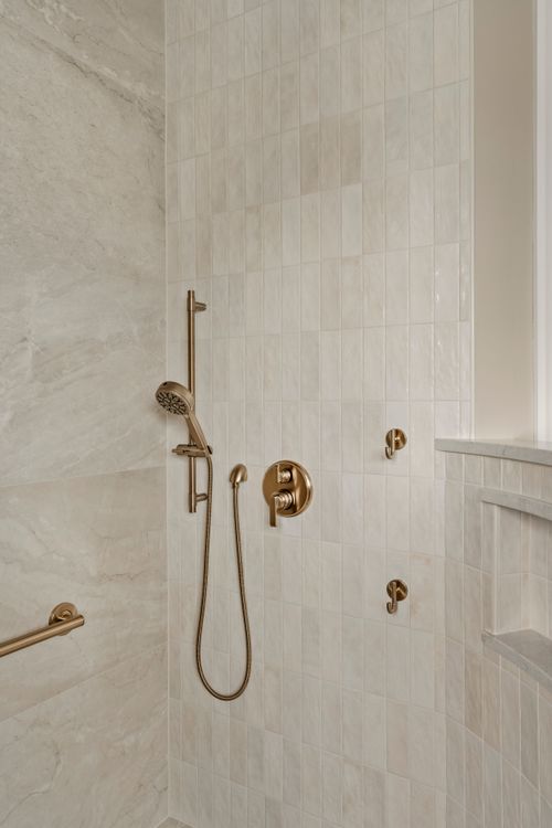 Brass handheld shower fixture on a slide bar mounted in a tiled shower