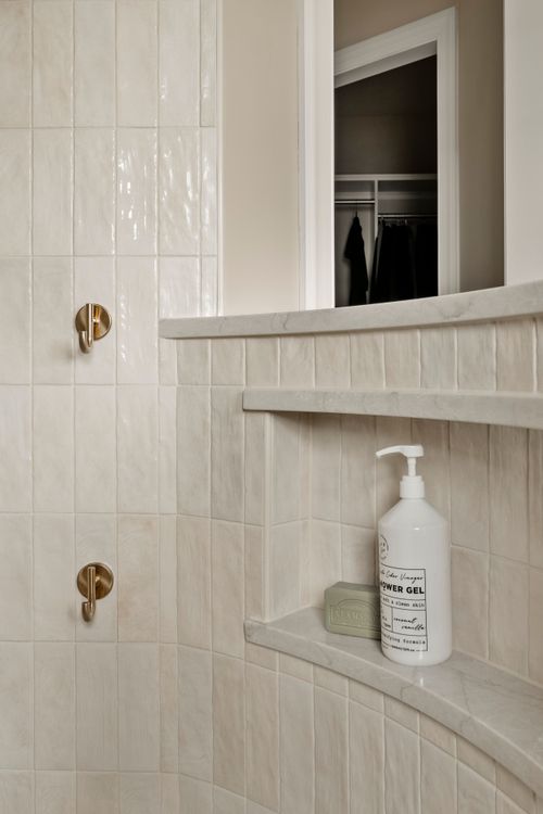 Close view of brass wall hooks in a shower with a closet doorway visible beyond