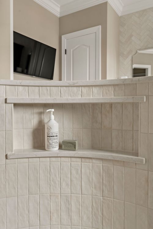 Curved marble shower shelf with soap and shower gel below a wall-mounted television