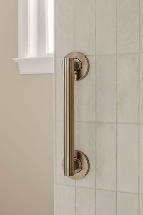 Close view of a brass shower door handle against a tiled wall near a window