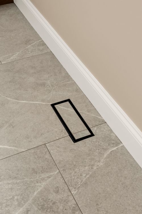 Floor outlet cover set into patterned tile flooring near a baseboard