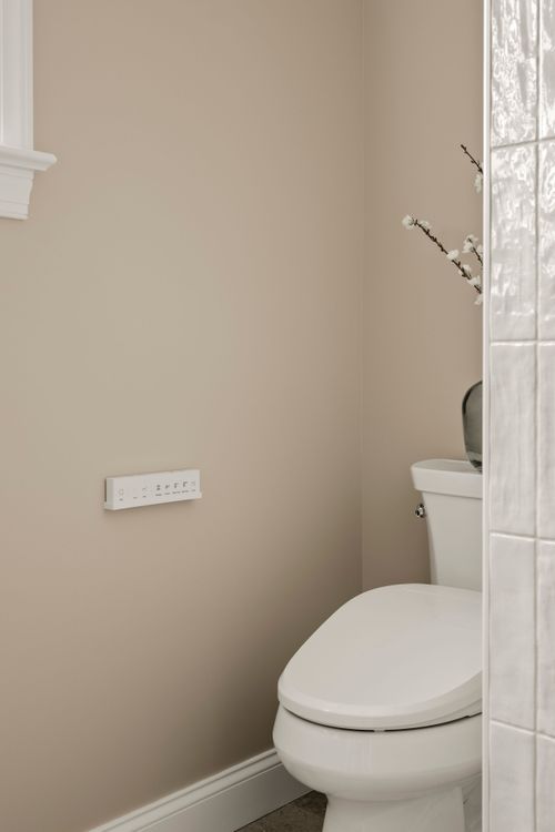 Toilet nook with tile walls, a wall-mounted control panel and a vase of branches