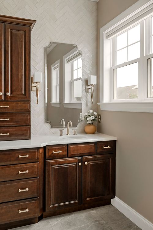 Tall dark wood linen cabinet flanked by brass wall sconces against herringbone tile