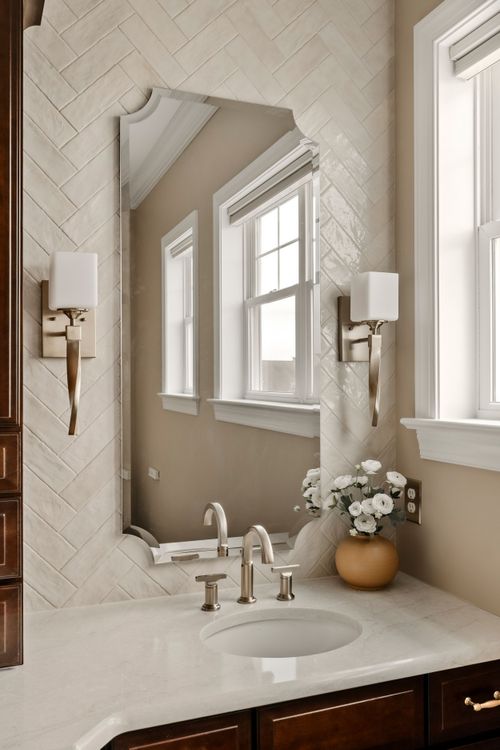 Bathroom vanity with a dark wood linen tower and herringbone tile backsplash near a window