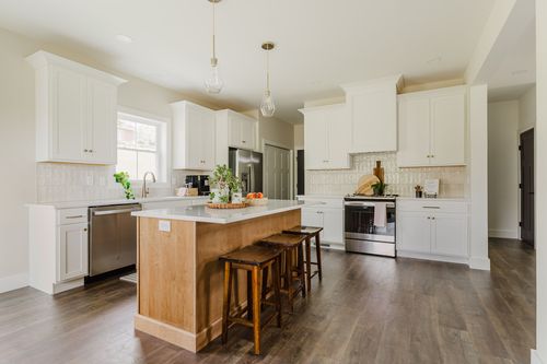 White kitchen with wood island seating three, stainless fridge and range
