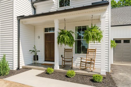 Close-up covered porch entrance with hanging ferns, rocking chairs and house number above the door