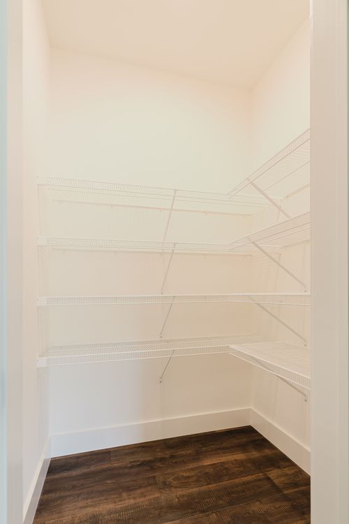 Empty white walk-in closet with wire shelving and dark wood flooring