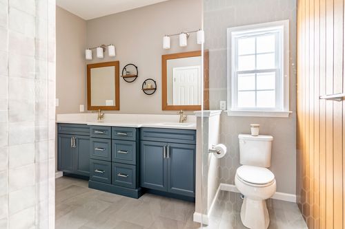 Double vanity bathroom with navy blue cabinets, wood-framed mirrors and round wall shelves