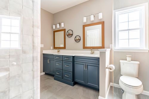 Double vanity with navy blue cabinetry and wood-framed mirrors beside a window