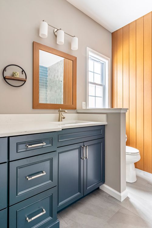 Blue vanity with a wood-framed mirror beside a toilet nook and wood plank wall