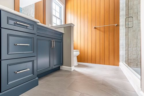 Blue vanity with brushed nickel hardware beneath a wood-framed mirror and round wall shelves