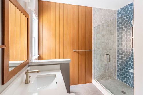 Bathroom vanity with a wood-framed mirror across from a wood plank wall and glass shower