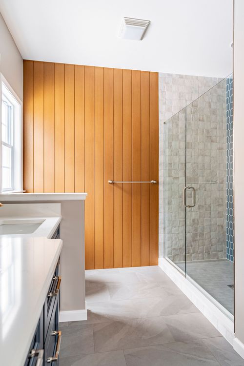 Wood plank accent wall with a towel bar beside a tiled walk-in shower