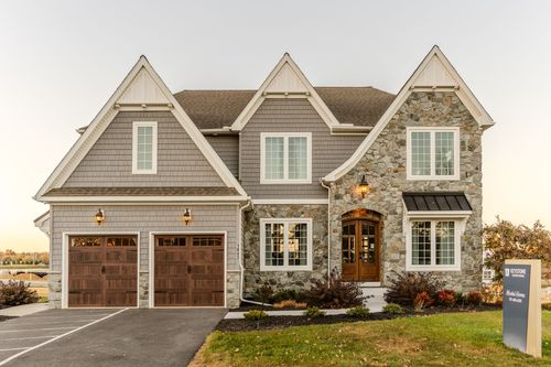 Stone and shingle two-story custom home exterior with a three-car garage at dusk
