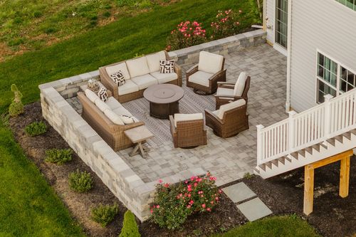 Aerial view of a paver patio with wicker seating and a fire pit table beside the home