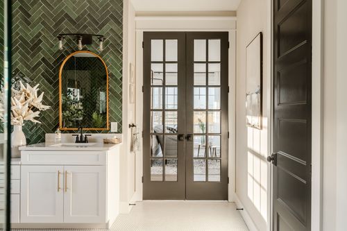 Hallway with black French doors opening to a bathroom, wood vanity in the foreground