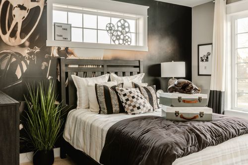 Bedroom with black accent wall, film-reel themed art and stacked vintage suitcases