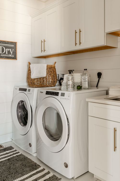 Laundry room with white cabinetry, front-load washer and dryer and a woven basket