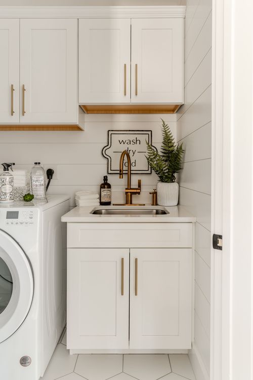 Laundry room sink with brass faucet, white cabinetry and a wash-dry-fold sign