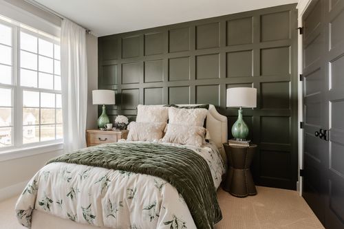 Bedroom with olive green paneled accent wall, green glass lamps and floral bedding