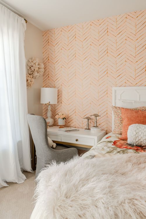 Kids bedroom with peach herringbone wall, white bed and layered orange pillows
