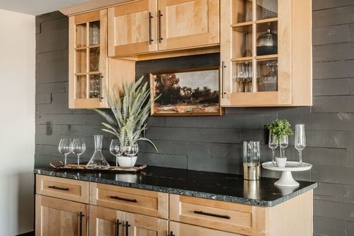 Wet bar detail with wood cabinetry, black countertop and glassware display