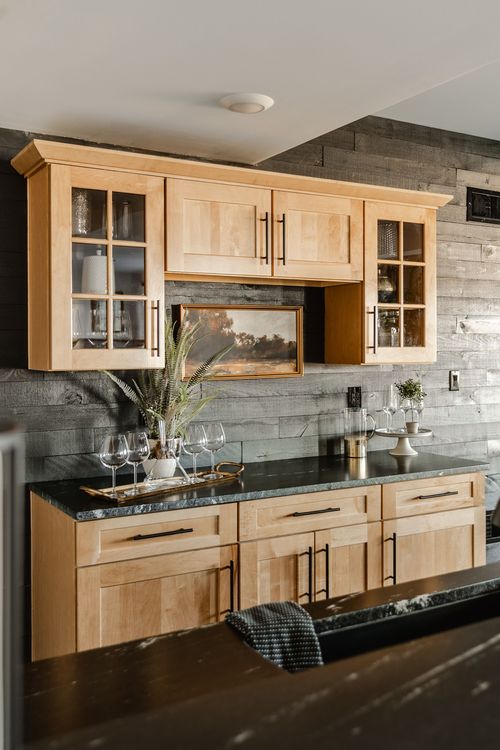Wet bar with wood cabinets, black countertop and framed landscape art