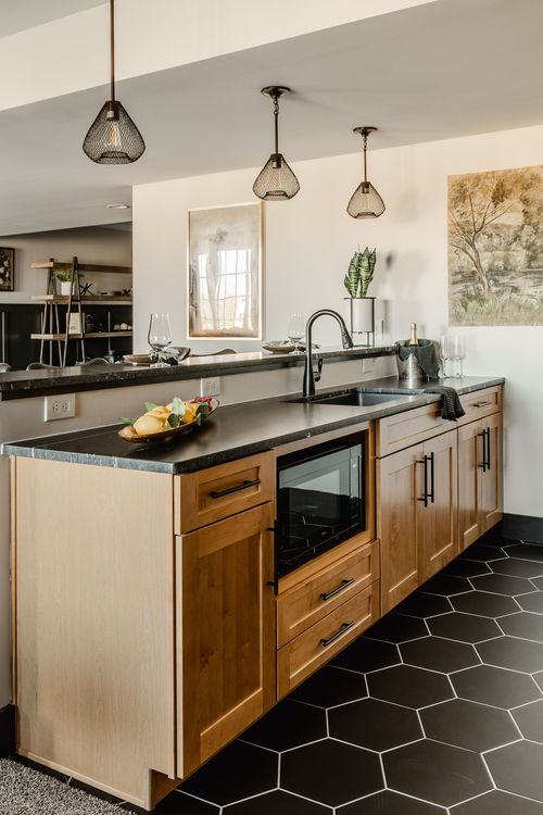 Basement kitchenette with wood cabinets, black hexagon tile and pendant lighting