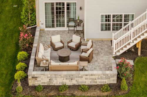Aerial view of a paver patio with wicker furniture and a fire table beside a staircase