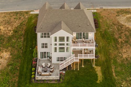 Aerial rear view of a large custom home with wraparound decks and a stone patio