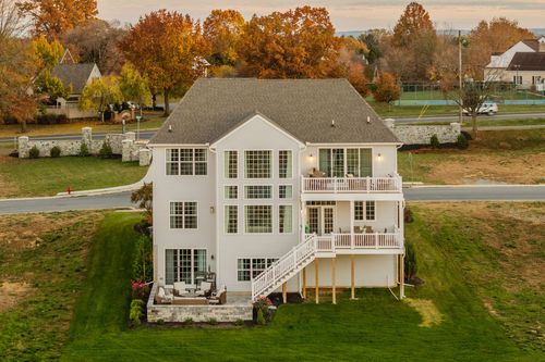 Aerial rear view of a large stone home with multiple decks and a paver patio