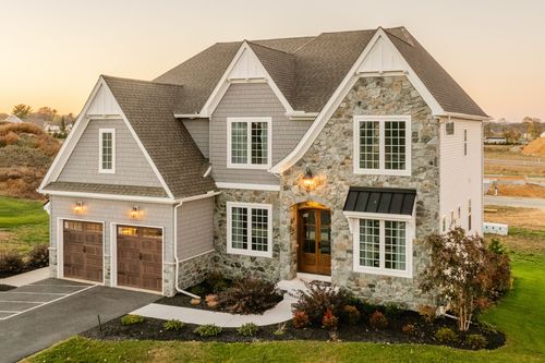 Front exterior of a two-story stone and shingle home with an arched entry and dormer windows