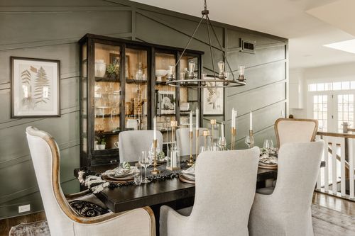 Dining room with a green paneled accent wall, upholstered chairs and a staircase view
