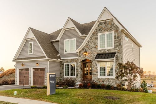 Front exterior of a custom stone home with a wood double door and gabled dormers at dusk
