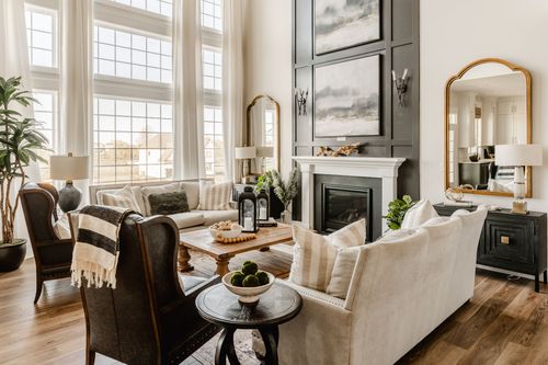 Living room with tall windows, layered seating and a black paneled fireplace wall