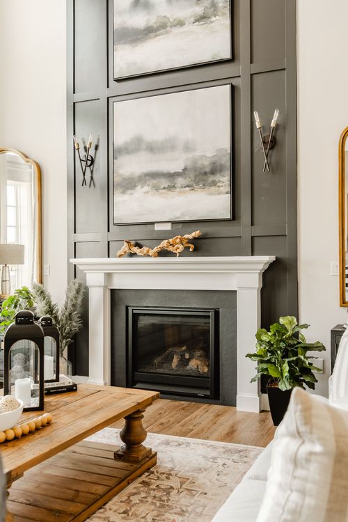 Living room with dark paneled fireplace wall, layered landscape art and white mantel