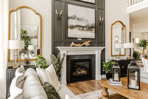 Living room with dark paneled fireplace wall, gold mirrors and layered landscape art