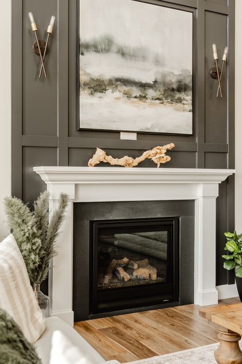Close-up of a dark paneled fireplace wall with layered landscape art and wood mantel