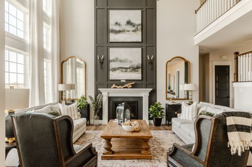 Two-story great room with a dark paneled fireplace wall flanked by gold mirrors and leather chairs
