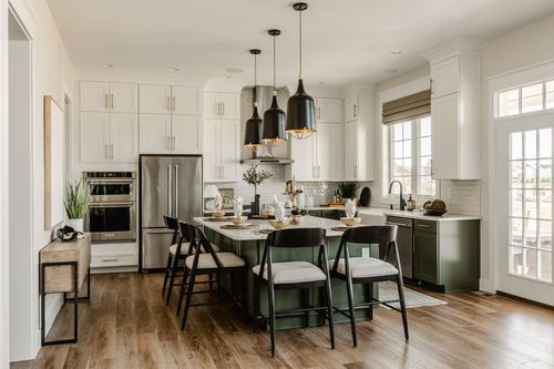 White kitchen with sage green island, black dome pendant lights and stainless appliances