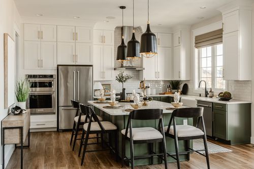 White and sage green kitchen with black pendant lights over a marble-look island