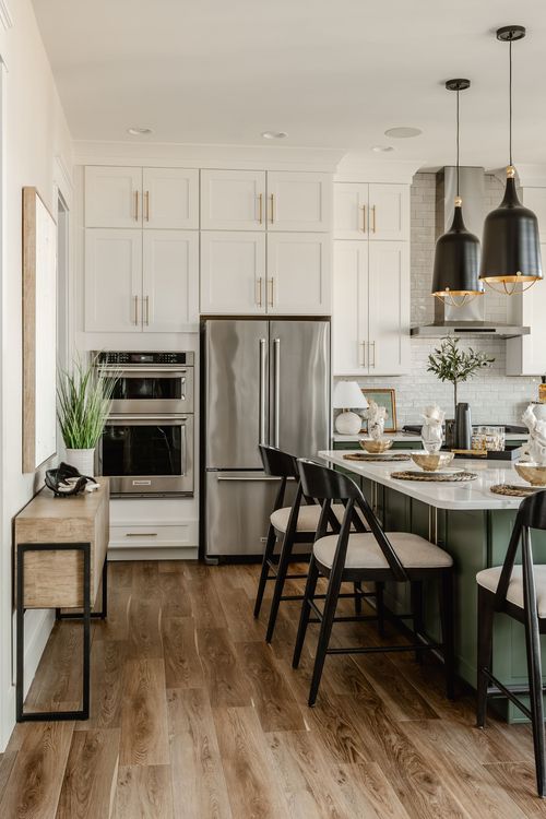 White kitchen with stainless double ovens, refrigerator and wood console table