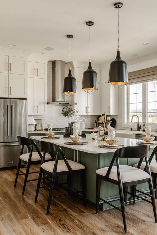Kitchen with sage green island, black pendant lighting and stainless steel range hood