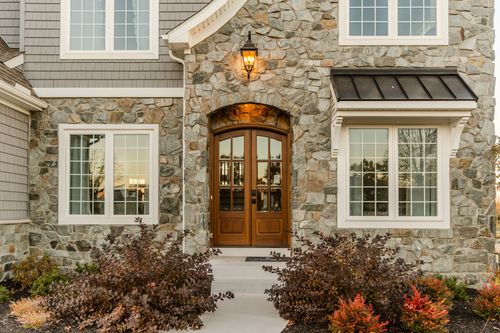 Stone facade with an arched wood front door flanked by white-trimmed windows