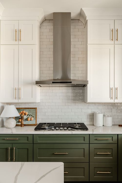 Kitchen cooktop with stainless range hood and tile backsplash flanked by white cabinets